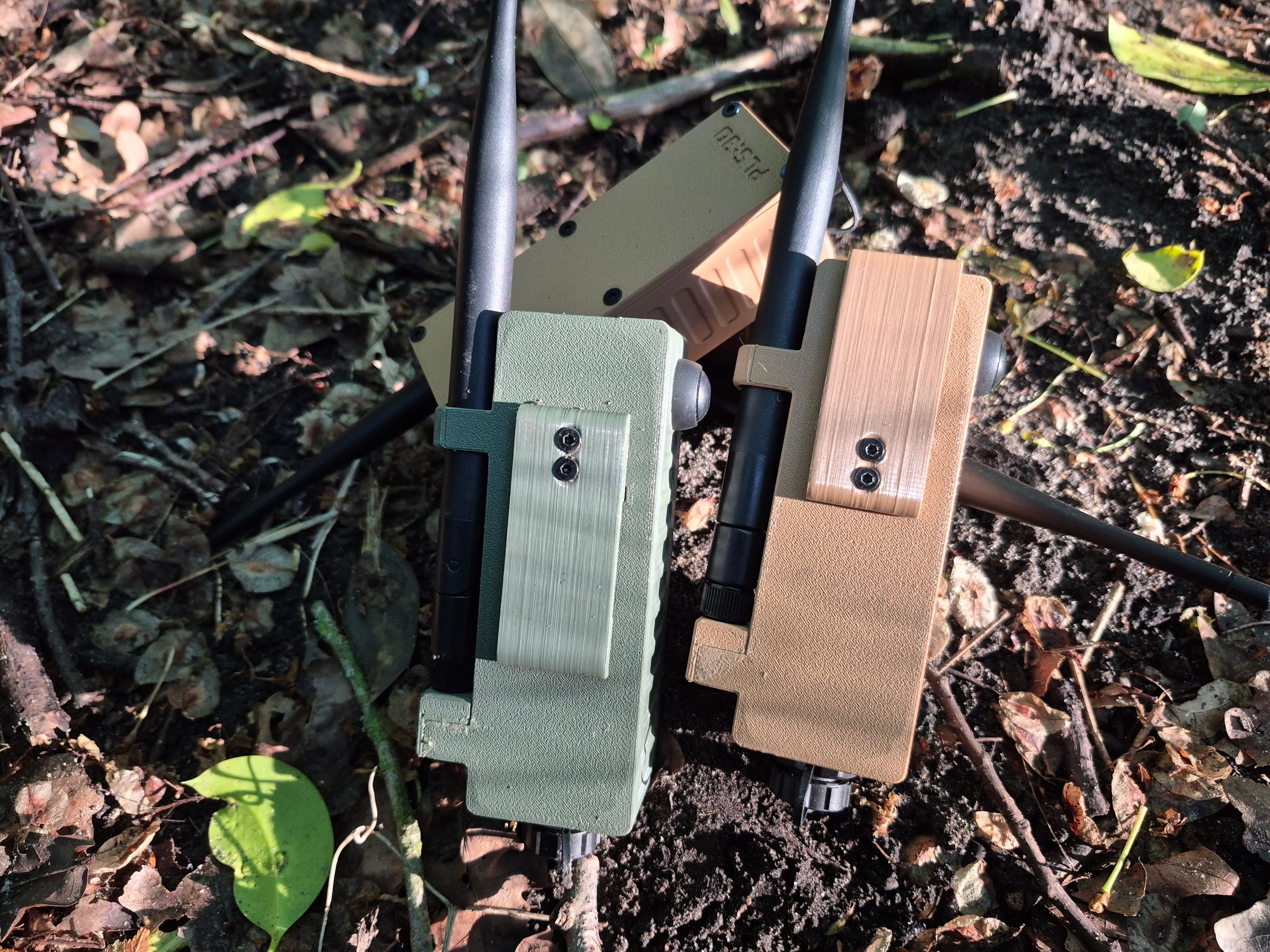 Olive and tan RBaken devices side by side with antennas in dry leaves