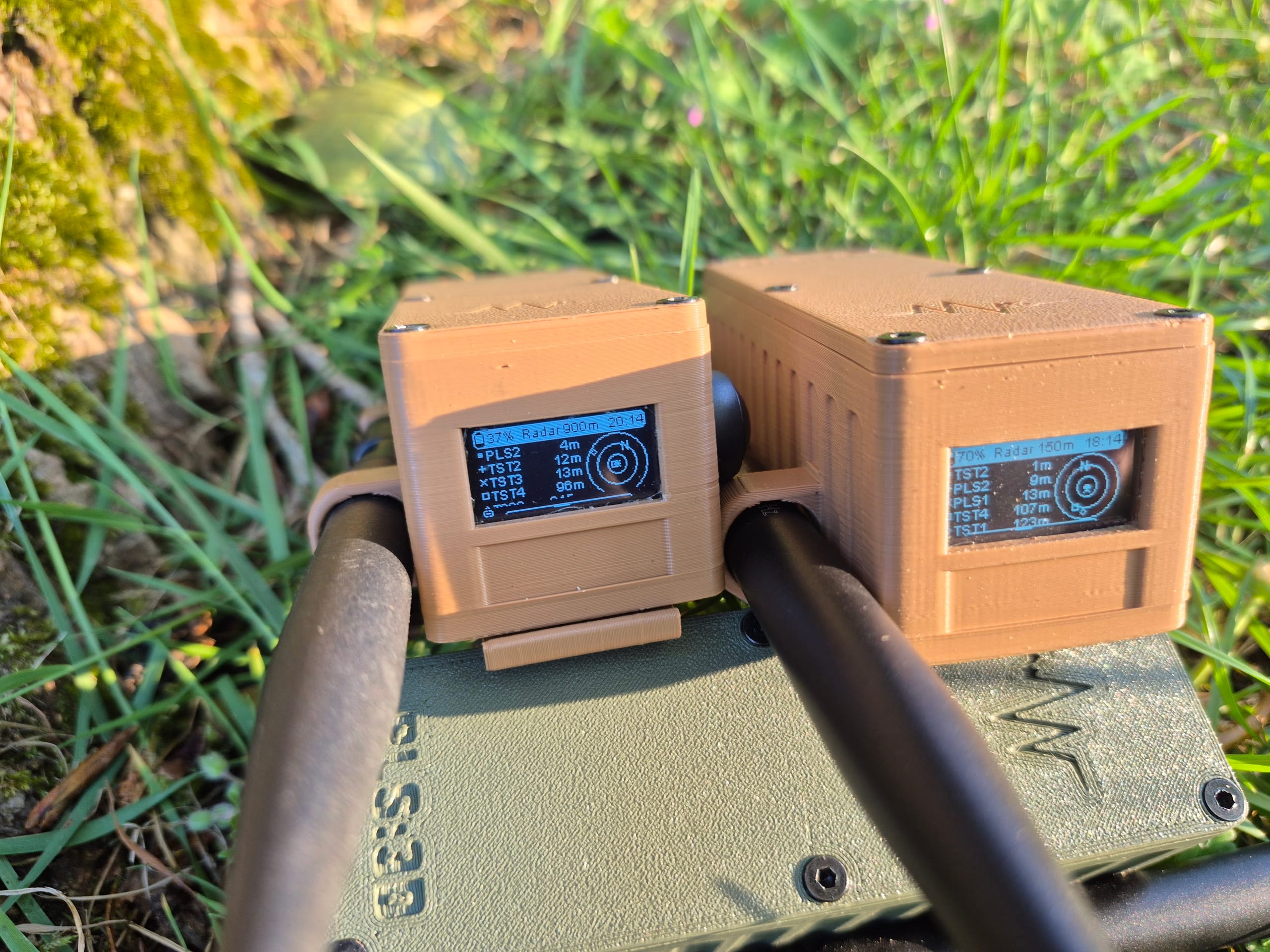 Two RBaken devices in grass with radar screens showing teammate distances