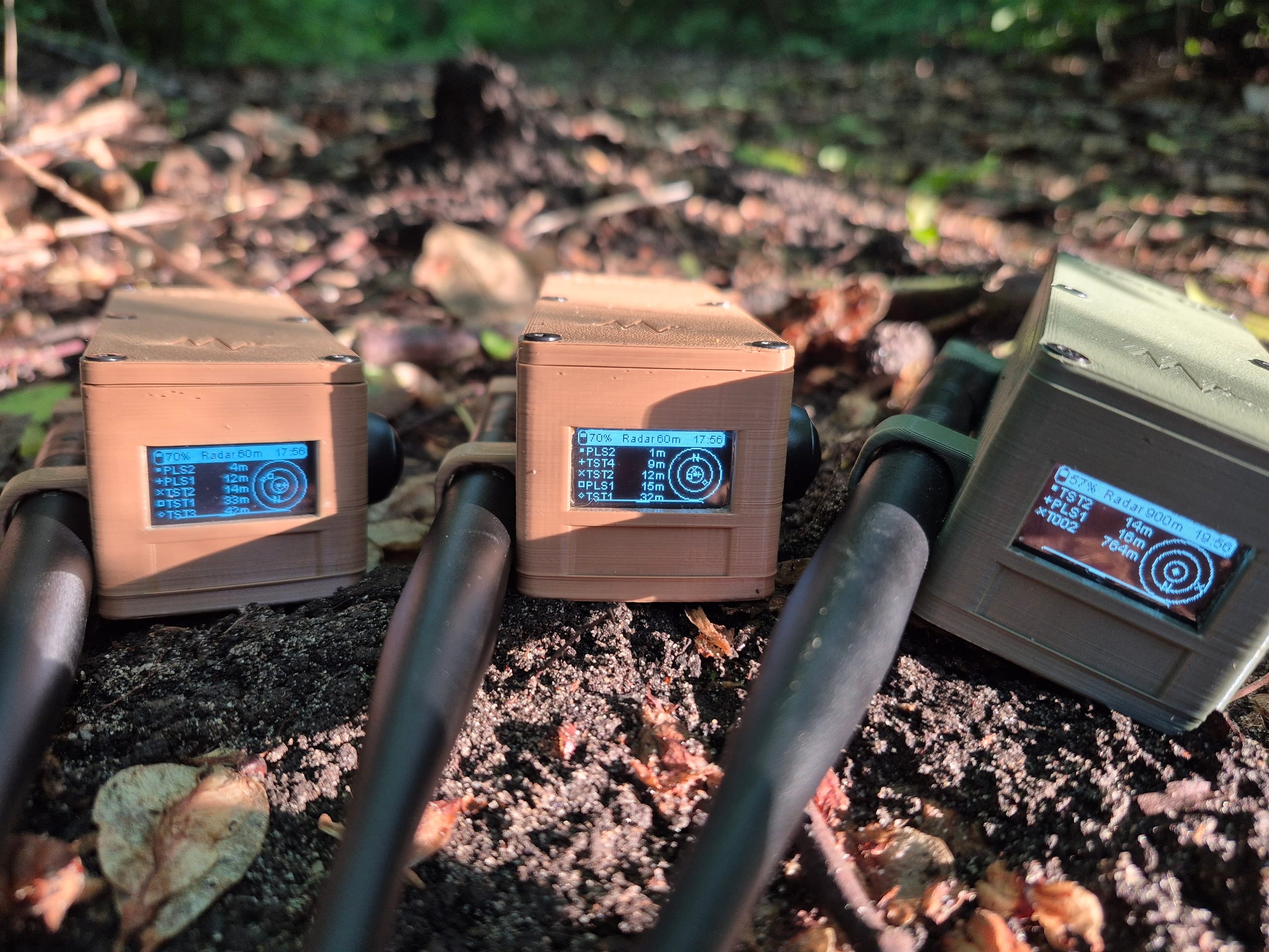 Three RBaken devices lined up in autumn forest leaves with radar screens lit